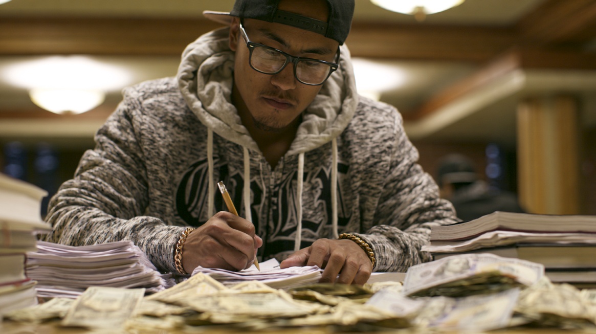 Student calculating finances at a desk with books, notes, and cash.